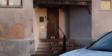 Entrance to a burned building with charred wooden beams, steps, and a police car in the foreground